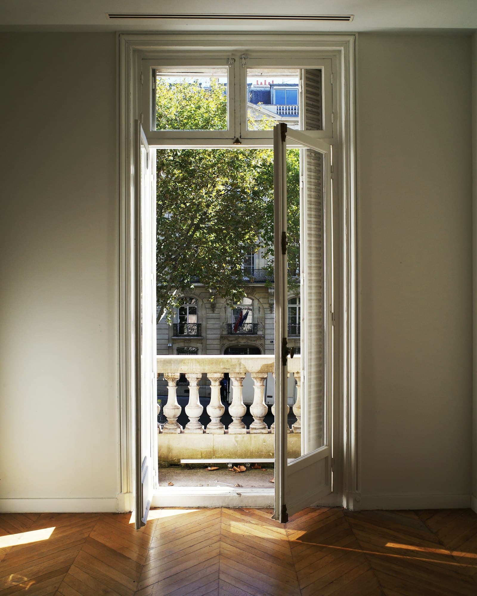 Una portafinestra aperta su un balcone con balaustra, il parquet a spina nella luce